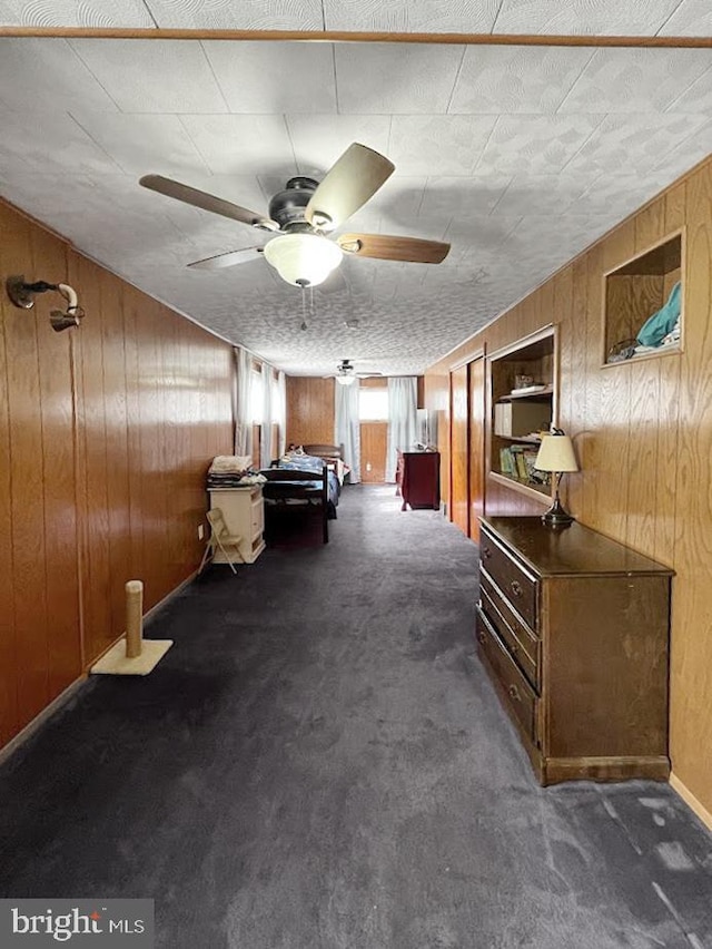 interior space featuring wood walls, dark carpet, and a ceiling fan