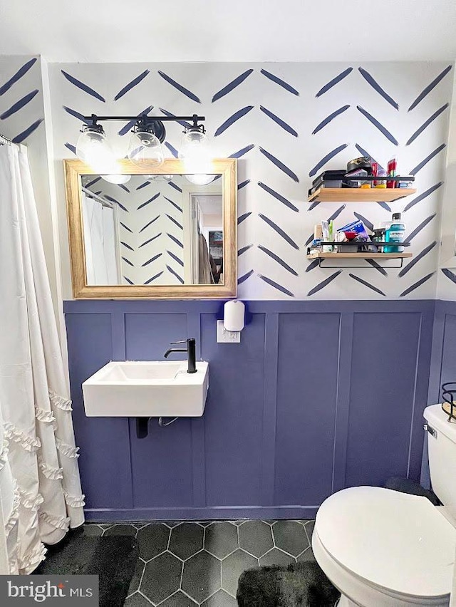 full bathroom featuring a wainscoted wall, a sink, a decorative wall, and toilet