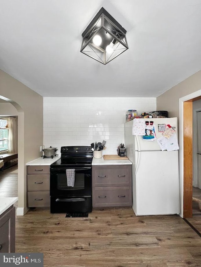 kitchen with dark wood-type flooring, light countertops, black electric range oven, and freestanding refrigerator