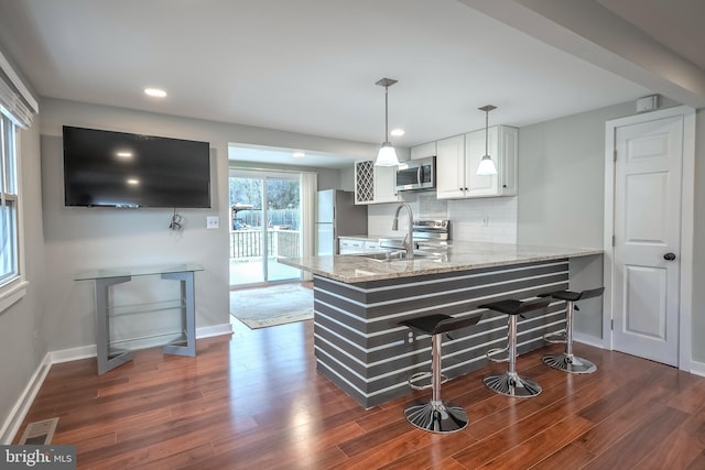 kitchen featuring a breakfast bar area, decorative backsplash, appliances with stainless steel finishes, white cabinetry, and a peninsula