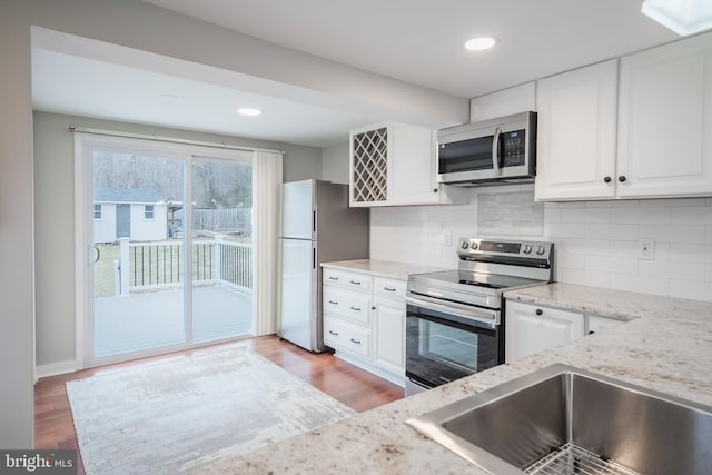 kitchen featuring stainless steel appliances, backsplash, white cabinetry, light stone countertops, and light wood-type flooring