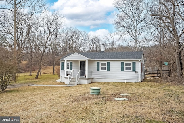 view of front of house with a shingled roof, a chimney, fence, and a front yard