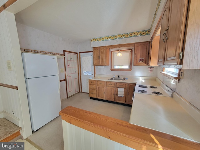 kitchen featuring light countertops, brown cabinetry, a sink, white appliances, and wallpapered walls