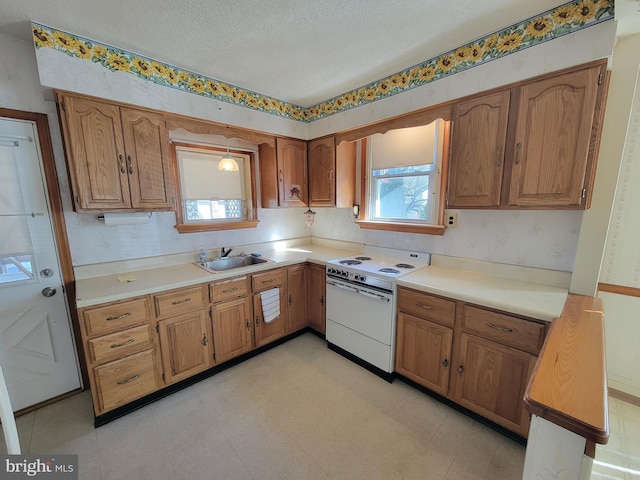 kitchen featuring white electric stove, a textured ceiling, a sink, light countertops, and brown cabinetry
