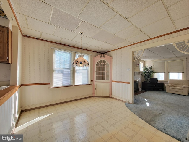 unfurnished dining area with wallpapered walls, a brick fireplace, light floors, and a wainscoted wall