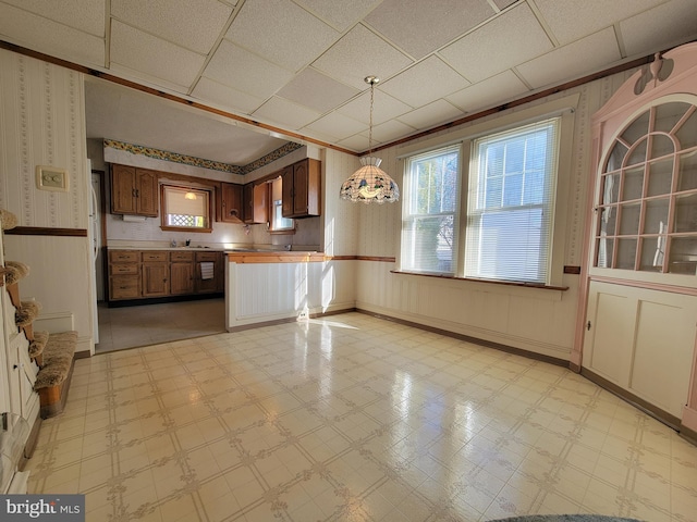 kitchen featuring a peninsula, wainscoting, a wealth of natural light, light floors, and wallpapered walls