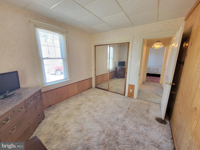 bedroom featuring a wainscoted wall, a closet, light carpet, and wooden walls