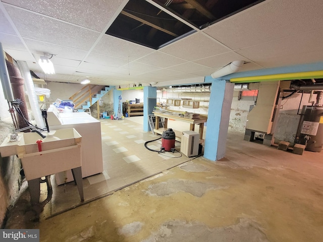 finished basement with stairs, a drop ceiling, washing machine and dryer, and electric water heater