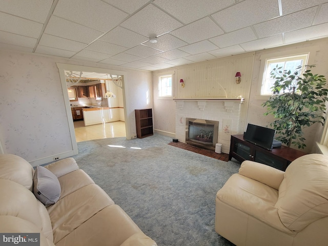 carpeted living area with a paneled ceiling, a brick fireplace, and baseboards