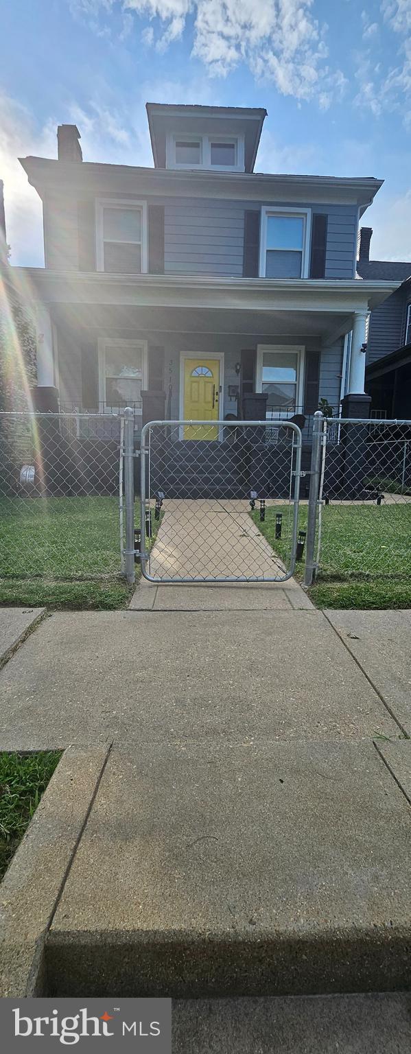 american foursquare style home featuring covered porch, a fenced front yard, and a gate