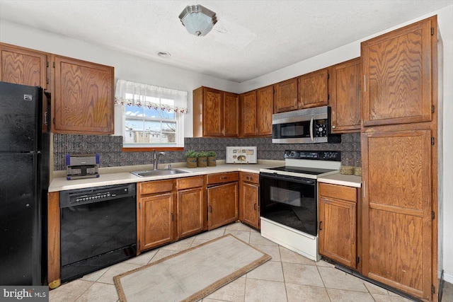 kitchen featuring light tile patterned floors, light countertops, brown cabinetry, a sink, and black appliances