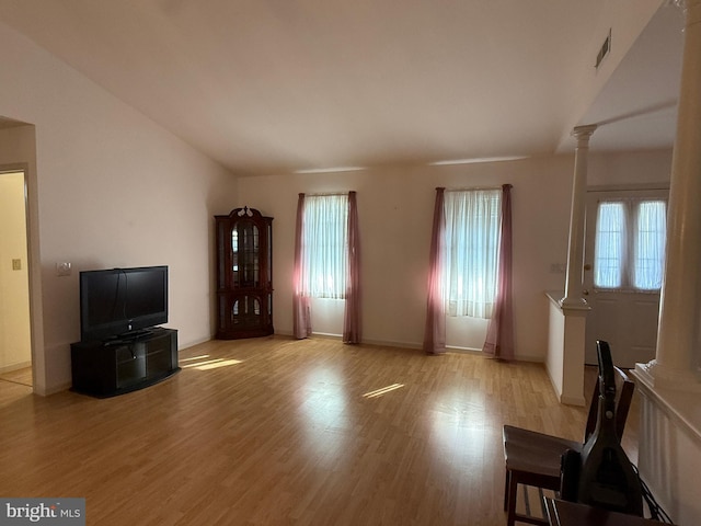 unfurnished living room featuring lofted ceiling, visible vents, light wood-style flooring, and ornate columns