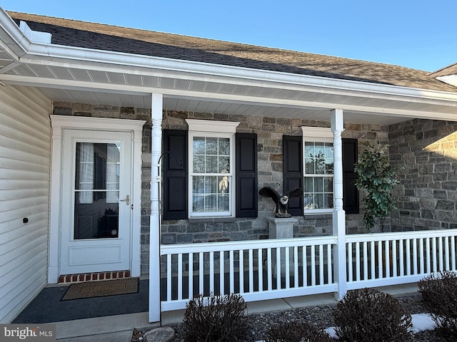 doorway to property with covered porch, stone siding, and a shingled roof