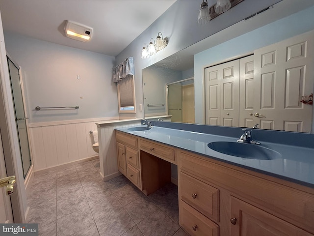 bathroom with wainscoting, a sink, toilet, and double vanity