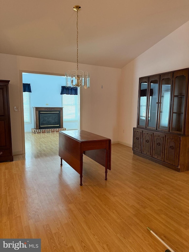 unfurnished dining area featuring a fireplace, light wood-style floors, vaulted ceiling, a chandelier, and baseboards