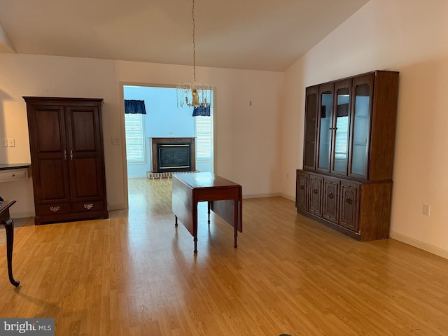 unfurnished dining area with lofted ceiling, a notable chandelier, baseboards, light wood-style floors, and a brick fireplace