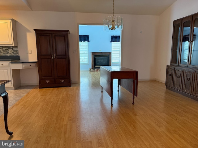 dining area featuring light wood-style floors, baseboards, a brick fireplace, and a chandelier