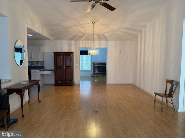 living room with light wood-type flooring, baseboards, vaulted ceiling, and ceiling fan with notable chandelier