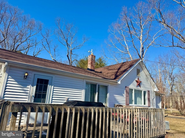 view of side of property with a shingled roof, a chimney, and a deck