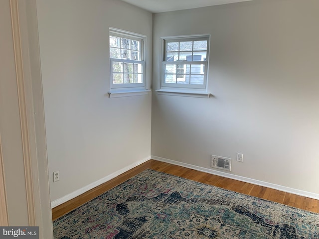 spare room with baseboards, visible vents, and wood finished floors