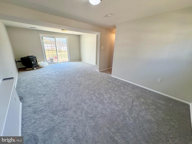 empty room with carpet, a wood stove, and baseboards