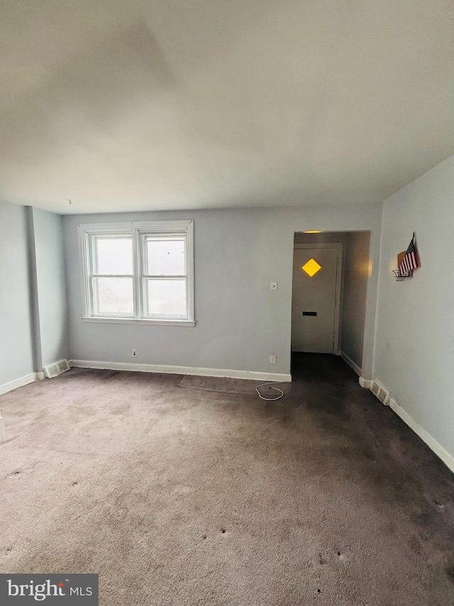 empty room featuring baseboards, visible vents, and dark carpet