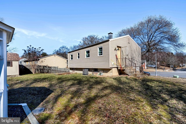 view of side of home with a yard, central AC, a chimney, and fence