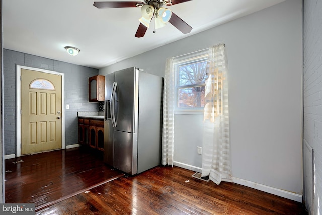 kitchen with brick wall, dark wood-style flooring, baseboards, light countertops, and stainless steel fridge with ice dispenser