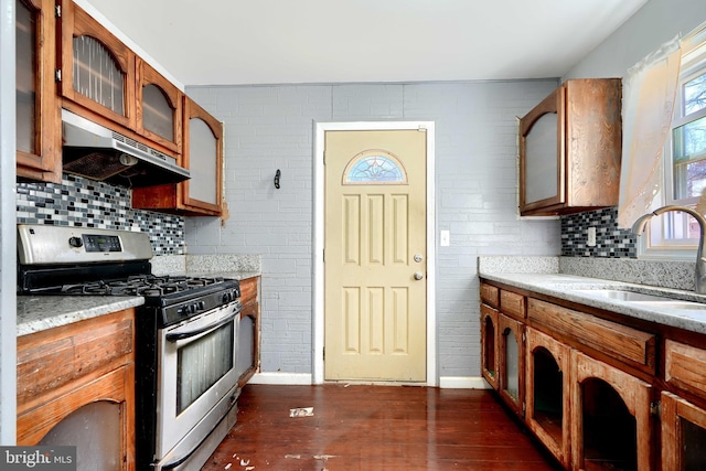 kitchen with decorative backsplash, dark wood finished floors, stainless steel gas range, under cabinet range hood, and a sink