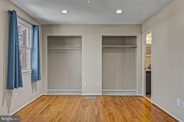 unfurnished bedroom with light wood finished floors, visible vents, baseboards, two closets, and recessed lighting