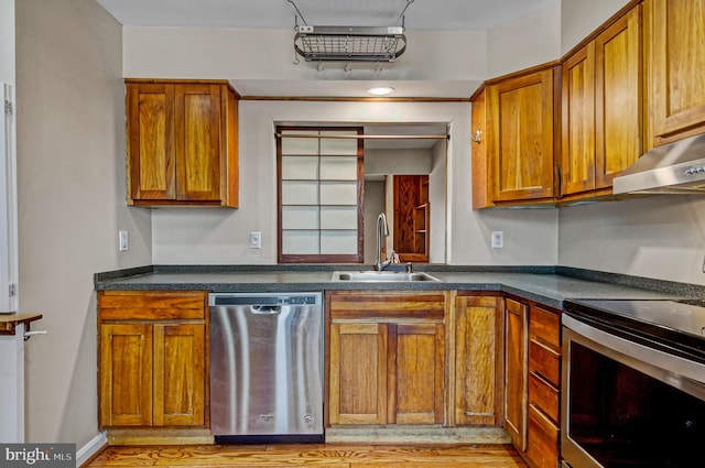 kitchen featuring under cabinet range hood, stainless steel appliances, a sink, brown cabinetry, and dark countertops