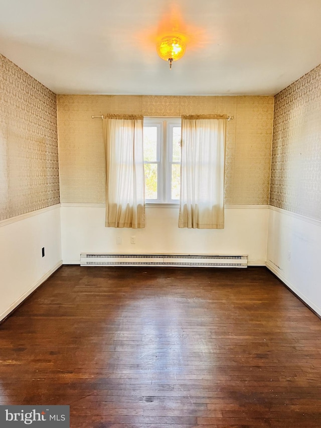 empty room featuring a wainscoted wall, dark wood-style flooring, and baseboard heating