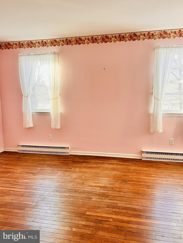 unfurnished room featuring wood-type flooring, baseboards, and a baseboard radiator