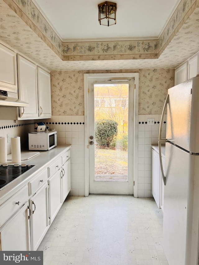 kitchen featuring a wainscoted wall, under cabinet range hood, wallpapered walls, white appliances, and light countertops