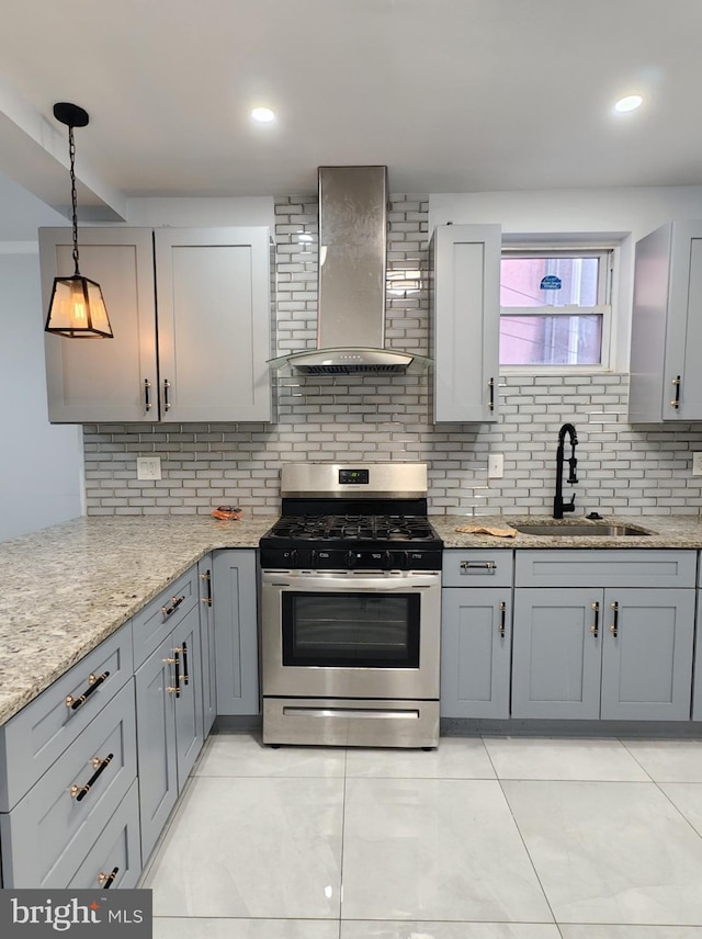 kitchen featuring decorative light fixtures, gray cabinets, gas stove, a sink, and wall chimney exhaust hood