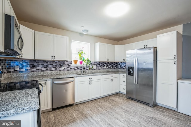 kitchen with stainless steel appliances, backsplash, white cabinetry, a sink, and light wood-type flooring