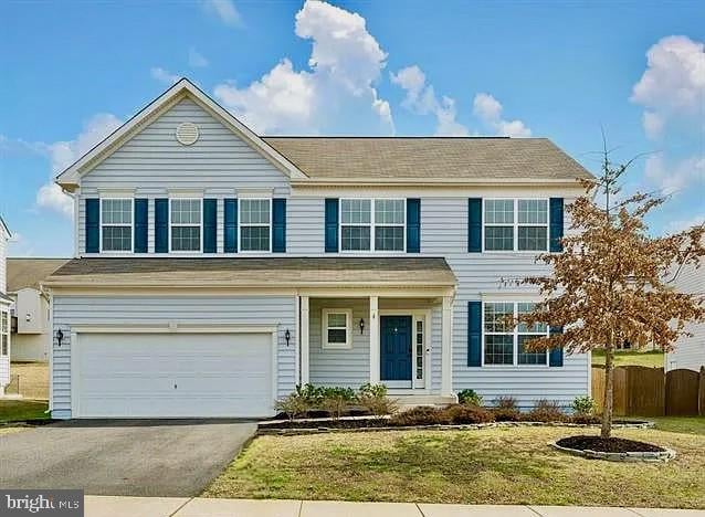 traditional-style home featuring a garage, driveway, a front lawn, and fence