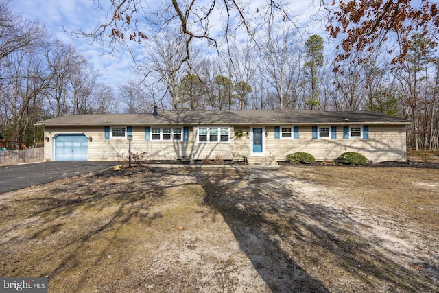 ranch-style house featuring a garage, entry steps, fence, and aphalt driveway