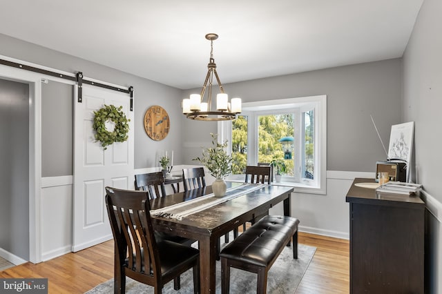 dining area with light wood-type flooring, a barn door, a notable chandelier, and wainscoting