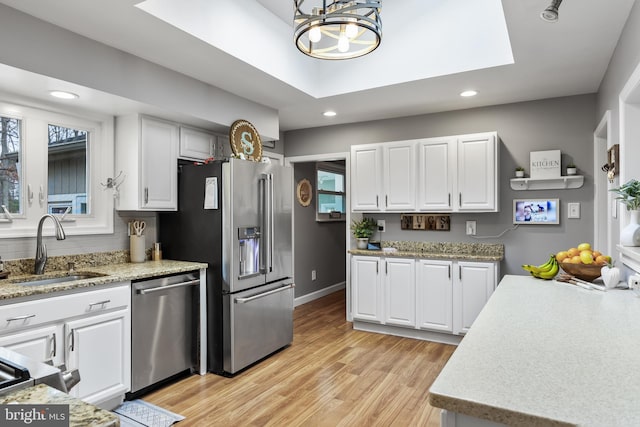 kitchen featuring appliances with stainless steel finishes, light wood-type flooring, white cabinets, and a sink