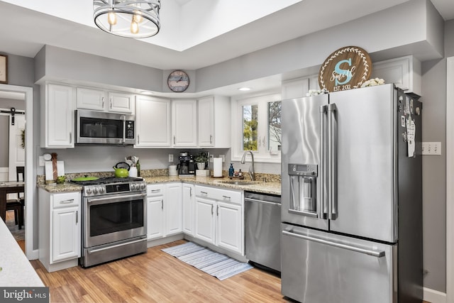 kitchen with appliances with stainless steel finishes, a barn door, light wood-type flooring, and white cabinets