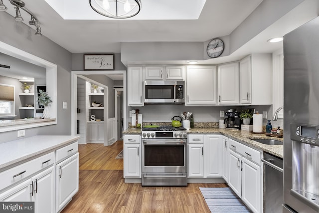 kitchen with light wood finished floors, light stone counters, stainless steel appliances, white cabinetry, and a sink