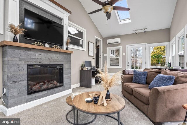 carpeted living area featuring baseboards, an AC wall unit, lofted ceiling with skylight, a glass covered fireplace, and track lighting