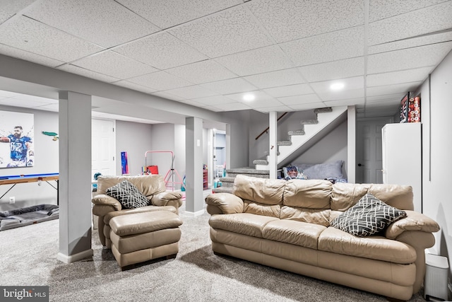 living room with stairs, a drop ceiling, and baseboards