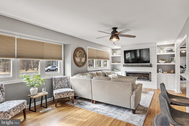 living area with a large fireplace, light wood-style flooring, a ceiling fan, and a wealth of natural light