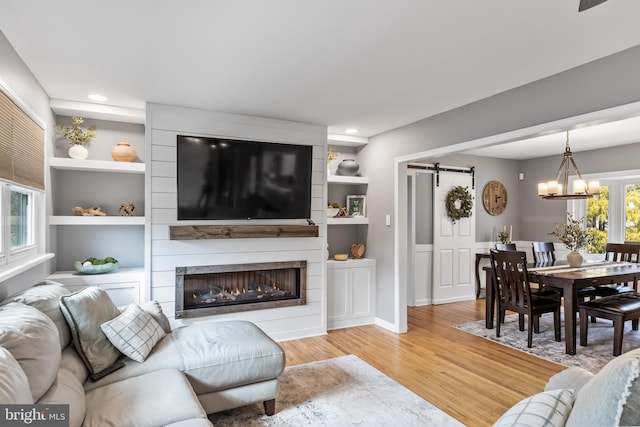 living area with built in shelves, a notable chandelier, light wood-style flooring, and a barn door