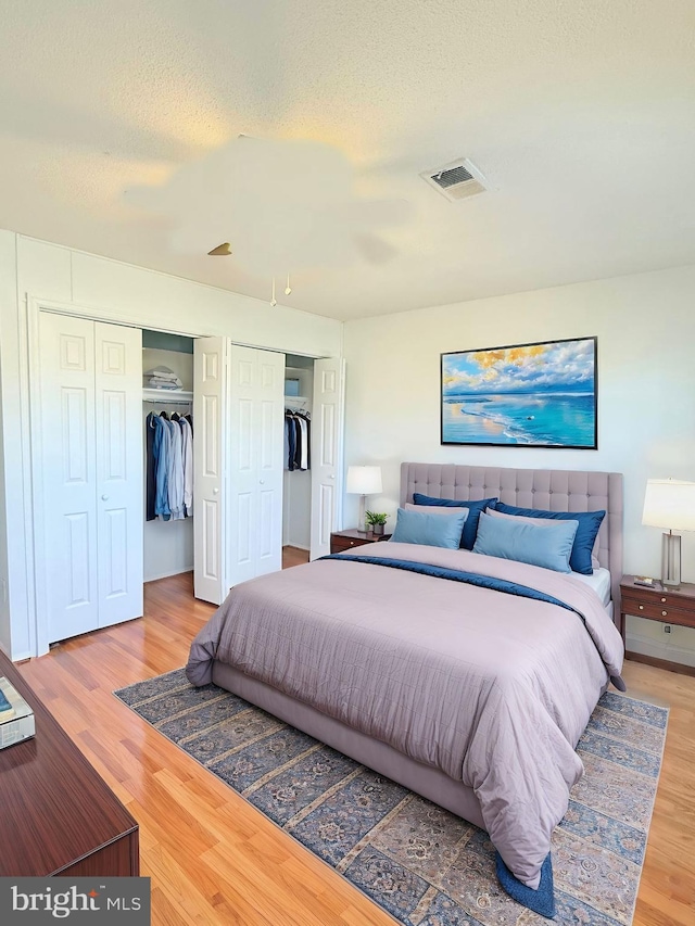 bedroom with a textured ceiling, visible vents, multiple closets, and wood finished floors