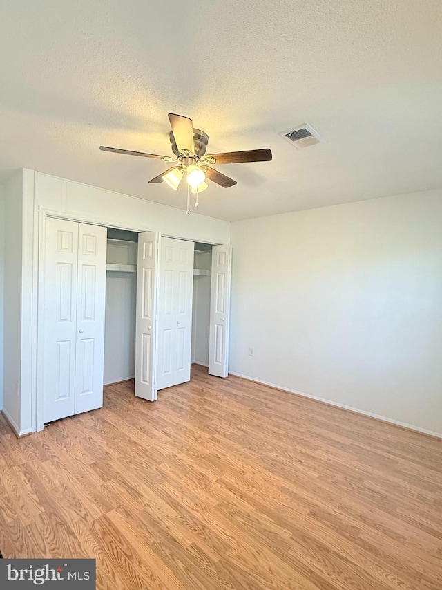 unfurnished bedroom featuring multiple closets, visible vents, a ceiling fan, a textured ceiling, and light wood-type flooring