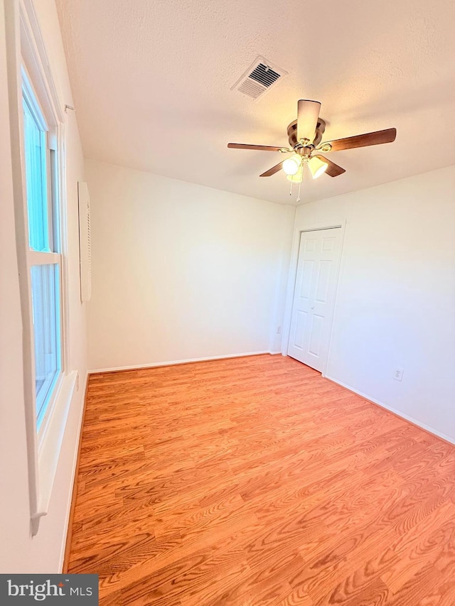 spare room featuring a textured ceiling, ceiling fan, wood finished floors, and visible vents