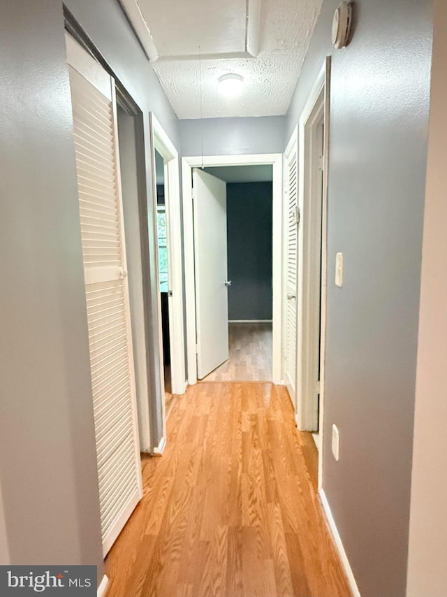 hall featuring light wood-style floors, attic access, baseboards, and a textured ceiling